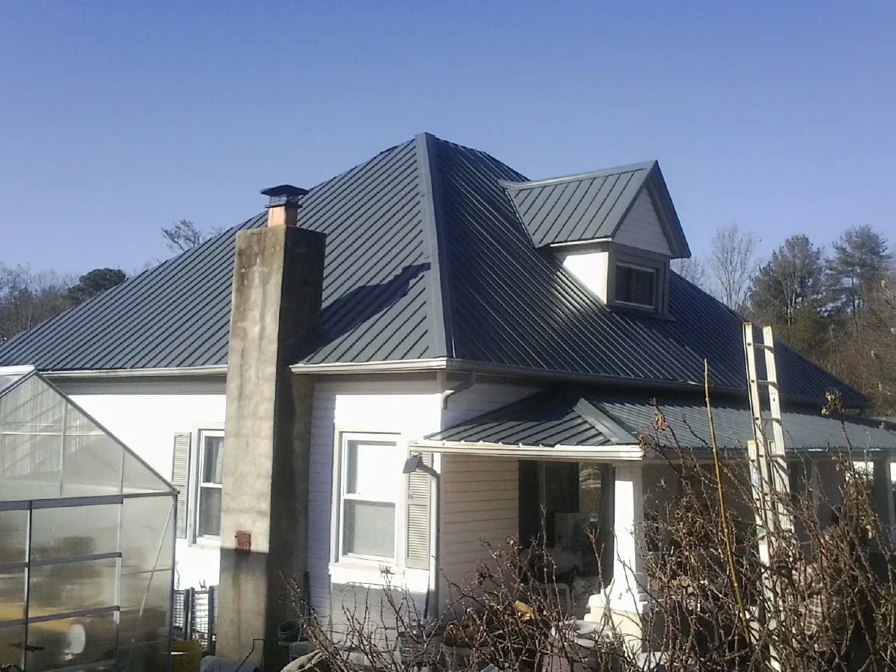 Dark blue standing seam metal roof on a white farmhouse with dormer — Slate & Tile Roof Repair by Roofing Brothers in Rose Hill