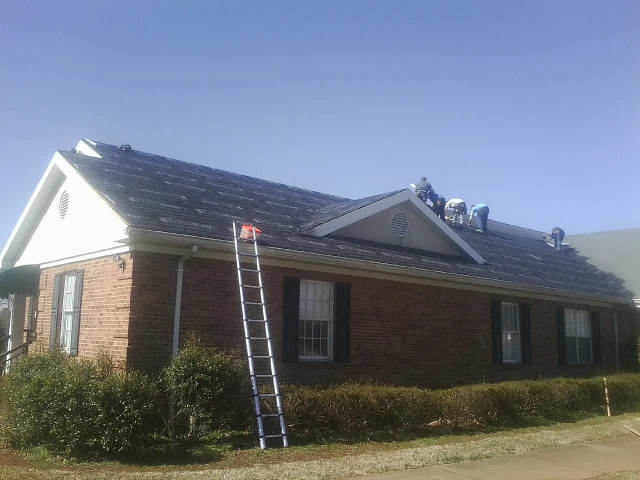 Crew tearing shingles off a brick ranch roof with a ladder set — Emergency Roof Repair work by our crew in Rose Hill
