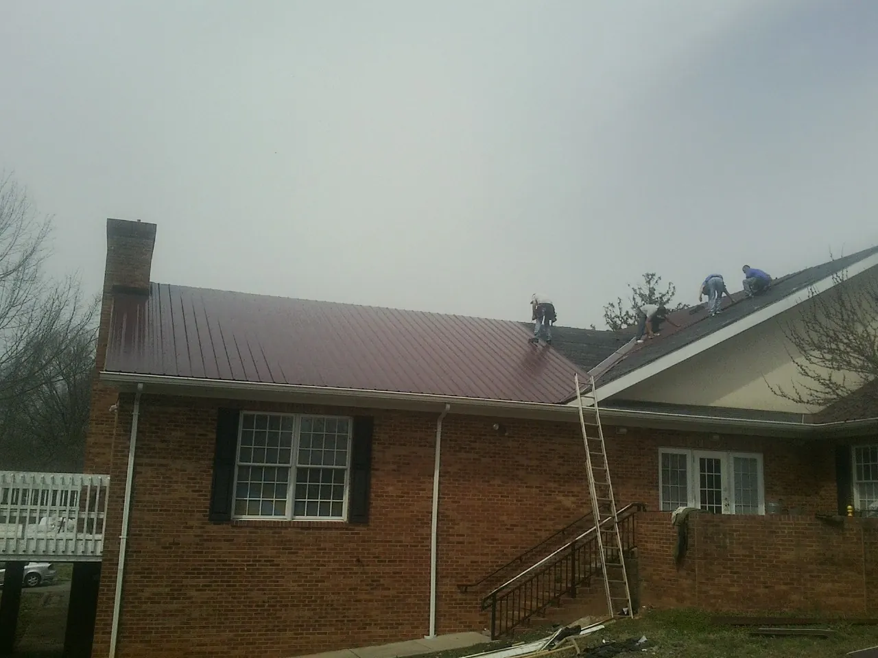 Crew setting red metal roofing panels on a brick home in Rose Hill