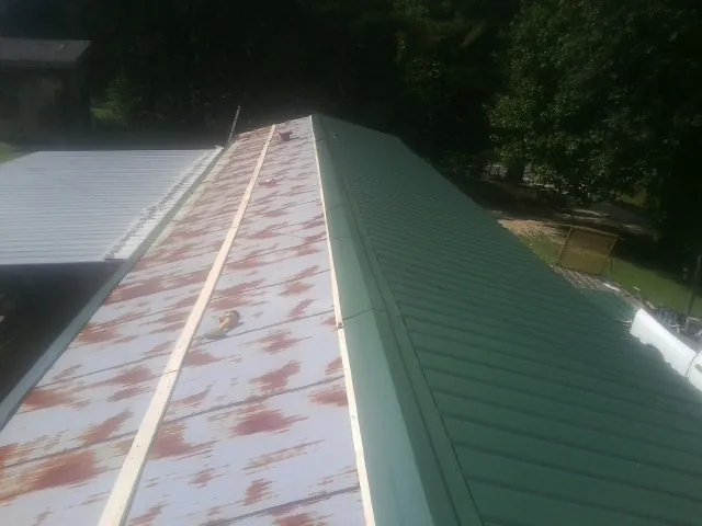 Old rusted panels beside newly installed green metal roofing — Wind Damage Roof Repair by Roofing Brothers in Rose Hill