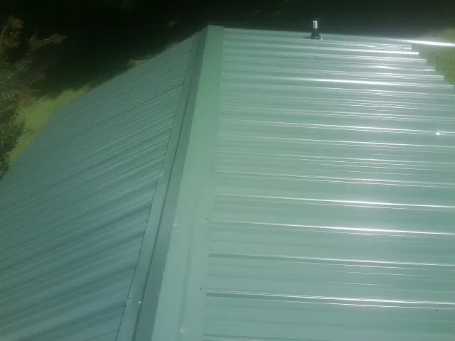 New green metal panels meeting at the ridge of a roof — Flat Roof Repair work by our crew in Rose Hill