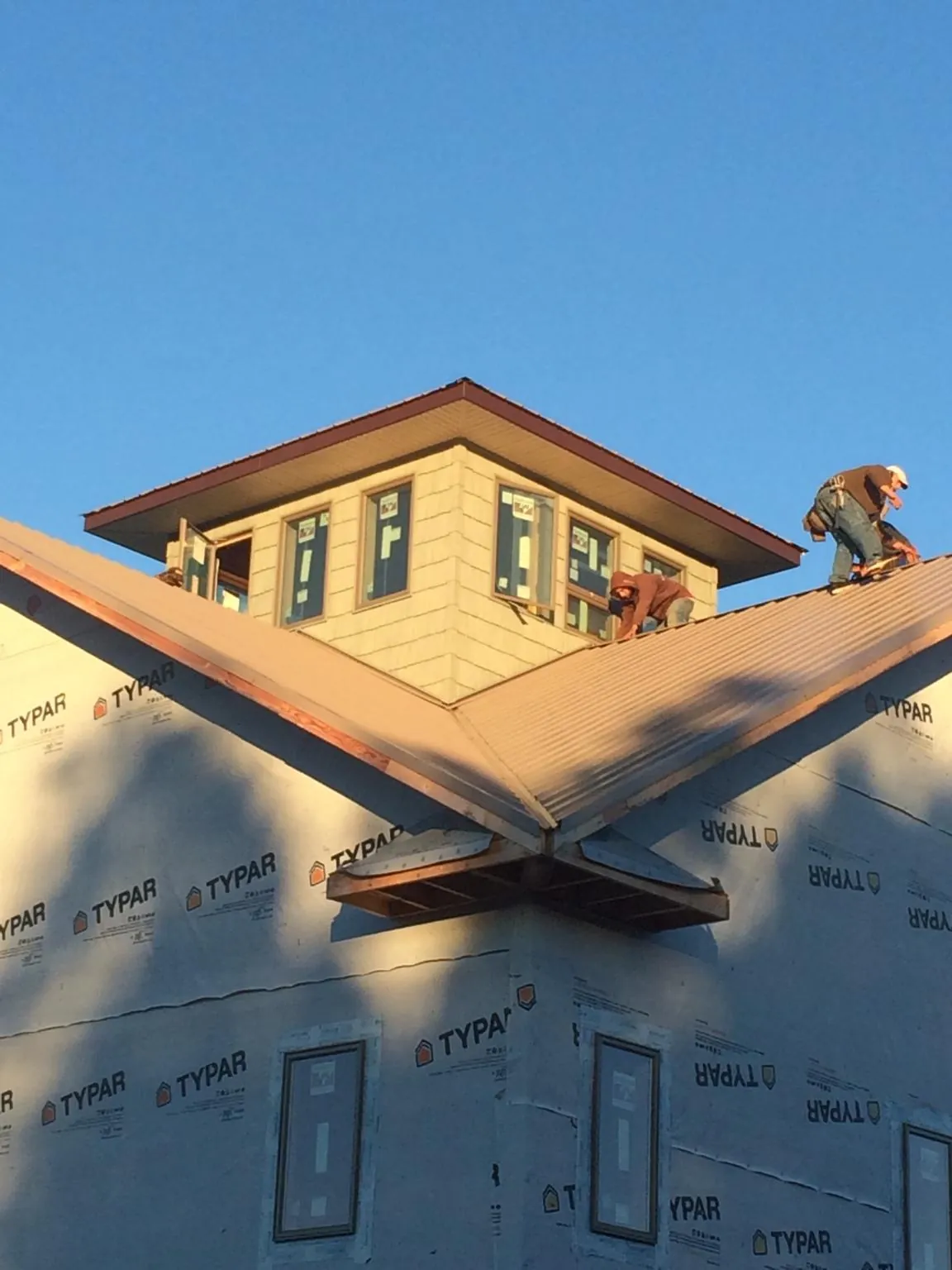 Roofers working around a rooftop cupola on a new metal roof at sunset — Roof Waterproofing in Rose Hill by Roofing Brothers
